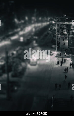 Fußgänger gehen auf einem städtischen Bürgersteig Stadt in der Nacht. Von einem hohen Aussichtspunkt genommen. Bild in schwarz-weiß Monochrom. Stockfoto