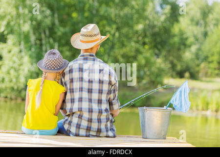 Rückansicht von Vater und Tochter sitzen auf der Brücke und Angeln Stockfoto