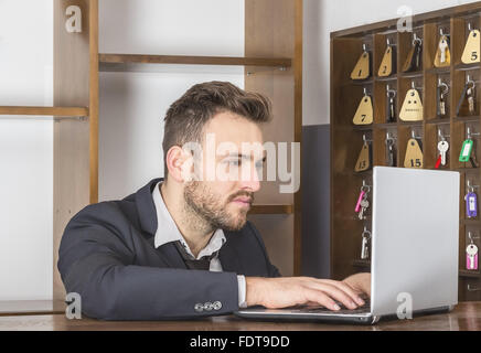 Eine Angestellte an der Rezeption arbeiten auf dem Laptop an seinem Schreibtisch in einem kleinen Hostel. Stockfoto