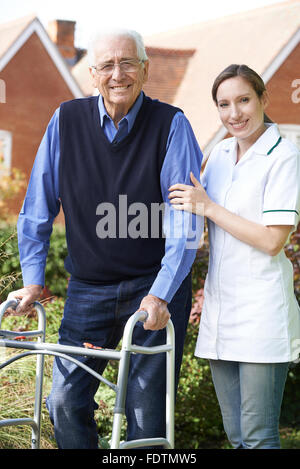 Pflegeperson Senior Menschen helfen, zu wandeln im Garten unter Verwendung des Rahmens zu Fuß Stockfoto