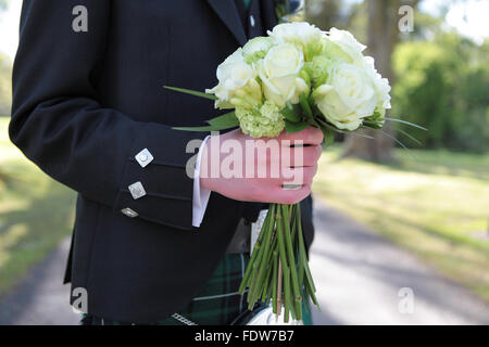 Bräutigam in traditionelle schottische Hochzeit Outfit hält die Bräute bouquet Stockfoto