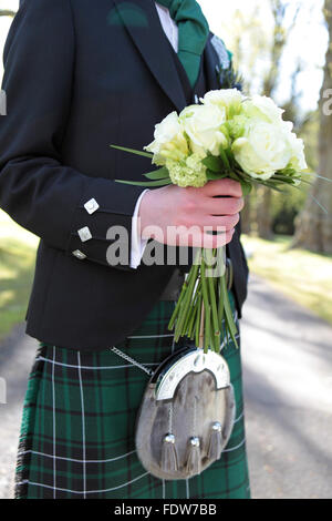 Bräutigam in traditionelle schottische Hochzeit Outfit hält die Bräute bouquet Stockfoto