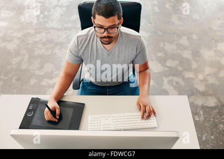 Hohen Winkel Bild des jungen Mannes mit einem Stift und Tablett während der Arbeit an seinem Computer. Grafik-Designer arbeiten an seinem Schreibtisch. Stockfoto