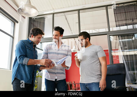 Junges Team von kreativen Menschen diskutieren Papierkram im Büro. Drei junge Männer, die im modernen Büro gehen durch einige Treffen tun Stockfoto