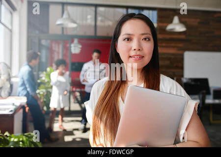 Porträt des jungen kreativen professionellen Betrieb Laptop im Büro. Junge asiatische Frau bei der Arbeit mit Kollegen diskutieren in backgr Stockfoto