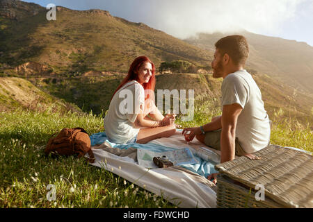 Junger Mann und Frau sitzen auf dem Rasen bei einem Picknick mit Glas Wein. Junges Liebespaar, ein Gespräch während auf Stockfoto