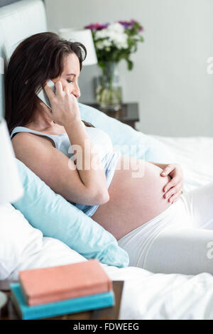 Schwangere Frau im Bett einen Anruf tätigen Stockfoto