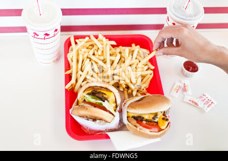 Eine Hand nimmt eine Pommes-frites aus einem Fach der Cheeseburger und Pommes frites warten darauf, bei In-N-Out Burger, Los Angeles, Kalifornien gegessen werden Stockfoto