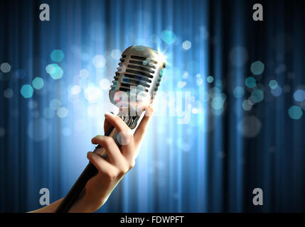 Weibliche Hand, die ein einziges Retro-Mikrofon vor bunten Hintergrund Stockfoto