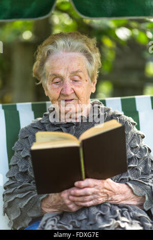 Eine ältere Frau liest das Buch in der Laube sitzen. Stockfoto