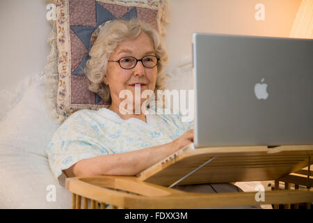 Ältere Frau im Bett mit Notebook-Computer. Stockfoto