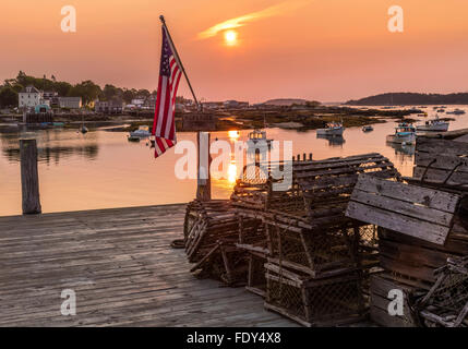 Stonington, ME: Amerikanische Flagge beleuchtet von Sunrise am Dock mit hölzernen Hummer fallen mit Blick auf Stonington Harbor Stockfoto