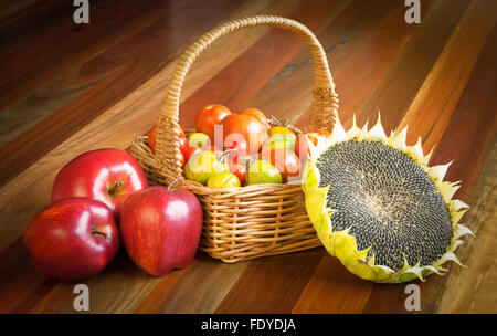Gesunde Rohkost Stilleben Komposition. Tomaten in einem Korb, reif Sonnenblume und drei rote Äpfel. Stockfoto