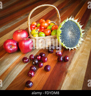 Kleine Tomaten, Kirschen, Äpfel und Reife Sonnenblume. Gesunde Bio-Lebensmittelzusammensetzung auf einem Holztisch Stockfoto