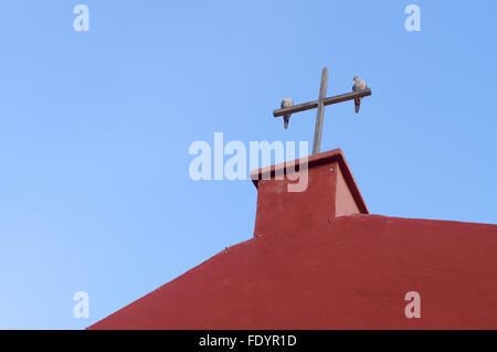 Zwei Tauben auf das hölzerne Kreuz der roten Kirche gegen blauen Himmel Stockfoto