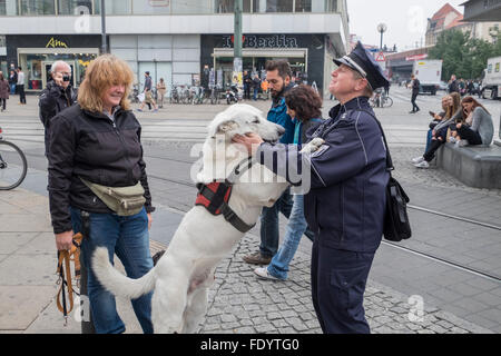 Ein weißer Schäferhund-Hund grüßt ein Polizist am Alexanderplatz, Berlin, Deutschland. Stockfoto