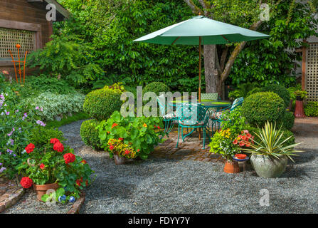Maury-Vashon Island, WA: Sommerterrasse umgeben mit Sommer Töpfe mit roten Geranien, Kapuzinerkresse und Yucca inmitten einer Cottage-Garten Stockfoto