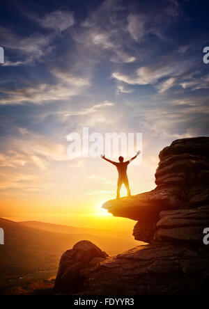 Eine Person, die sich von einem Höhepunkt, gegen Sonnenuntergang erreichen. Mit dem Ausdruck ihrer Freiheit Stockfoto
