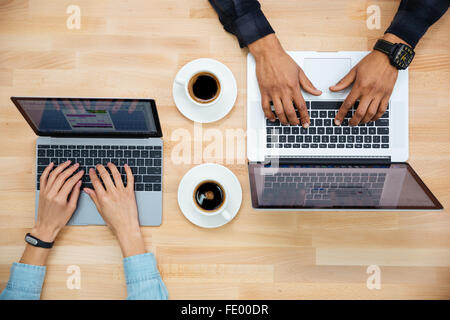 Draufsicht der Hände von Mann und Frau arbeiten mit zwei Laptops und Kaffeetrinken auf Holztisch Stockfoto