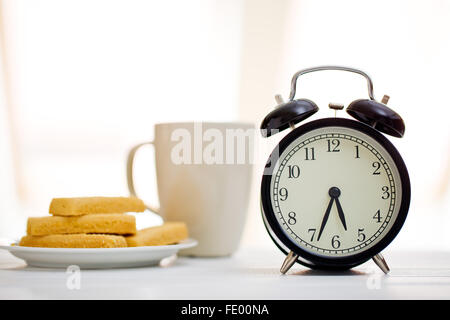 Wecker und Frühstück am weißen Tisch Stockfoto