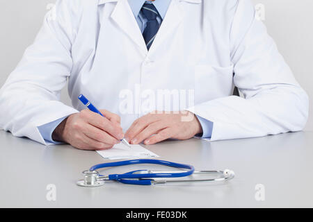 Arzt in seiner Ordination schreibt ein Rezept auf den Tisch. Stockfoto
