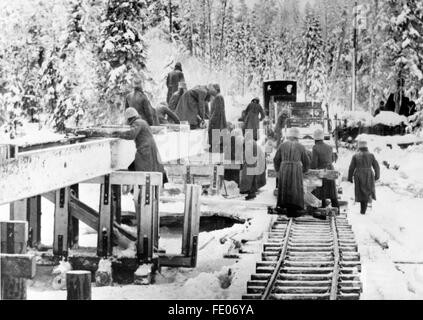 Das Nazi-Propagandafilm zeigt den Bau der Heeresfeldbahn (deutsche Feldbahn) durch die Todt-Organisation an der Ostfront. Das Foto wurde im Februar 1943 aufgenommen. Der Text der Nazi-Propaganda auf der Rückseite des Fotos lautet: "Soldaten und Männer der Todt-Organisation bauen die längste leichte Eisenbahn des Ostens im Karelischen Dschungel. Neben der im Bau befindlichen Brücke befindet sich ein zusätzliches Gleis, so dass das Material zum Arbeitsplatz transportiert werden kann.“ Fotoarchiv für Zeitgeschichtee - KEINE ÜBERWEISUNG - Stockfoto