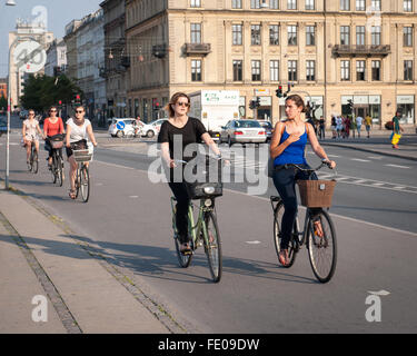 Junge dänische Frauen, die auf dem Dronning Louises Bro im sonnigen Kopenhagen, Dänemark, mit dem Fahrrad durch die Stadt fahren Stockfoto