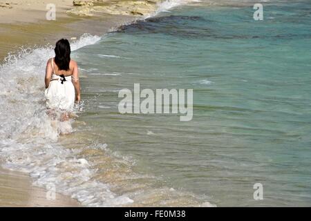 Frau im weißen Kleid zu Fuß in den tropischen Gewässern auf einem karibischen Strand. Stockfoto