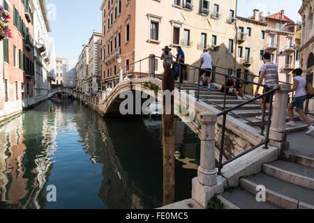 Touristen, die über eine der vielen kleinen Buckel Brücken in und um Venedig in Italien Stockfoto