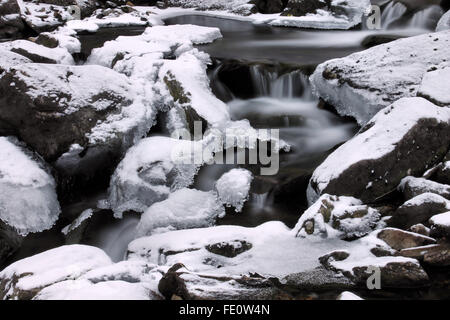 Eis und Schnee auf den Felsen in einem Bach im Ogwen Tal Stockfoto