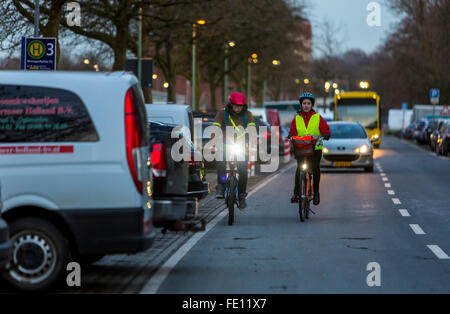 Radfahrer fahren, in der Dämmerung, in einer Stadtstraße, mit und ohne Beleuchtung und Sicherheitskleidung, Fahrrad Sicherheit, Sichtbarkeit bei Nacht Stockfoto