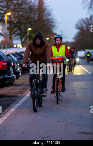 Radfahrer fahren, in der Dämmerung, in einer Stadtstraße, mit und ohne Beleuchtung und Sicherheitskleidung, Fahrrad Sicherheit, Sichtbarkeit bei Nacht Stockfoto