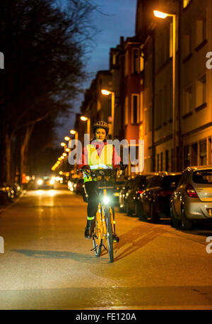 Radfahrer fahren, in der Dämmerung, in einer Stadtstraße, mit und ohne Beleuchtung und Sicherheitskleidung, Fahrrad Sicherheit, Sichtbarkeit bei Nacht Stockfoto