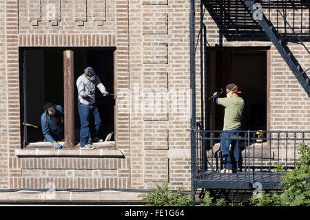 Zwei Bauarbeiter die Fenster aus einem Wohnhaus zu entfernen, während ihr Chef ihre Arbeit inspiziert Stockfoto