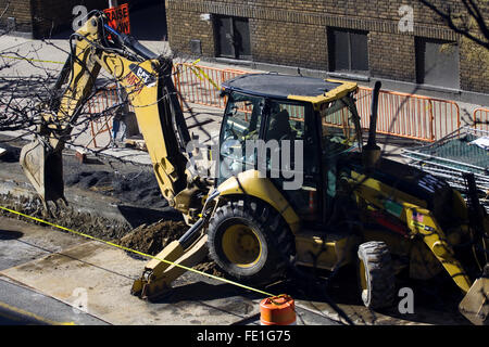 Bauarbeiter einen gelben Bagger gemacht durch die Caterpillar-Corporation, die auf einer Straße in New York City Graben ist in Betrieb Stockfoto