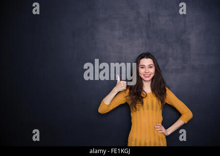 Lächelnde lässige Frau zeigt Daumen oben auf schwarzem Hintergrund Stockfoto
