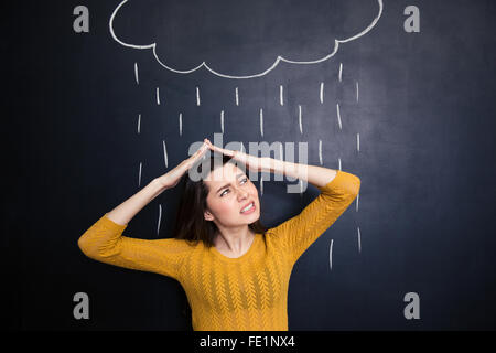 Verärgert junge Frau über den Kopf mit Händen von Regen auf Hintergrund der Tafel gezeichnet Stockfoto