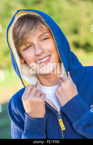 Glücklich lachende männliche junge blonde Teenager Kind außerhalb in Sommersonne tragen eine blaue hoody Stockfoto