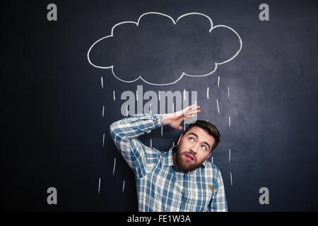 Unglückliche Jüngling versteckt aus Regenwolke und Regen über ihn auf einer Tafel Hintergrund gezeichnet Stockfoto