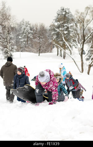 UFA - Russland 16. Januar 2016 - Kinder genießen den frischen Schnee mit improvisierten Folien und Schlitten hinunter Schnee Banken in Stockfoto