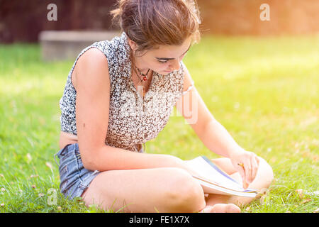 Teenager-Mädchen machen hier Hausaufgaben sitzt in einem Garten Stockfoto