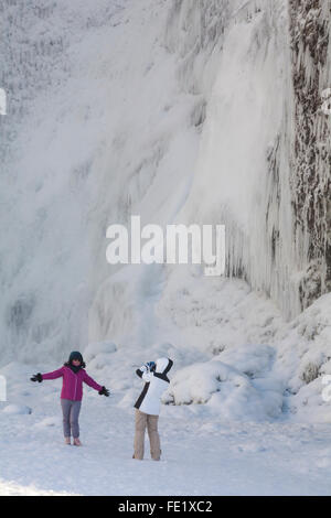 Junge Frau mit Foto am Skogafoss Wasserfall im Winter-Wunderland mit gefrorenem Wasser und Eiszapfen Island im Januar Stockfoto