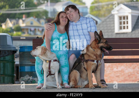 Blinde paar umarmt einander mit ihren Service-Hunde entspannen bei einer Bank am Strand Stockfoto