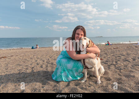 Junge Frau mit Sehbehinderungen und ihre Service-Hund umarmt am Strand Stockfoto