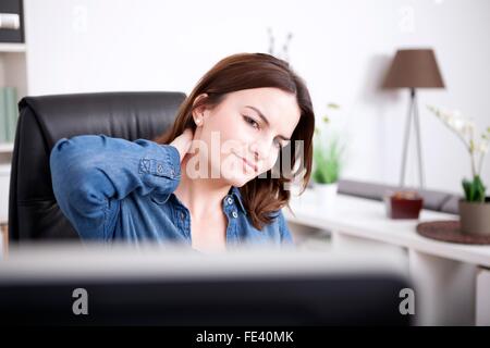 Schließen Sie sich müde Büro Frau sitzen im Büro, halten den Rücken von ihrem Hals während der Suche auf dem Computer-Monitor. Stockfoto