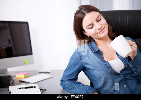 Bedauernd Geschäftsfrau in ihre leere Kaffeetasse suchen, als sie an ihrem Schreibtisch sitzt, nach dem Genuss einer entspannten Kaffeepause Stockfoto