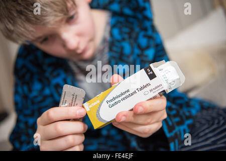 Schlecht weiße Teenager in seinem Schlafrock, öffnen ein Paket von Steroid Pillen für sein asthma Stockfoto