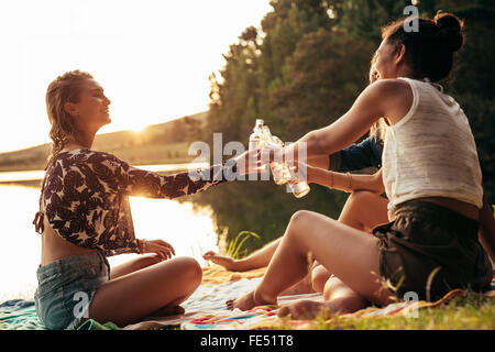 Gruppe junger Frauen, die an einem See zu feiern. Junge Freunde sind einander mit Bier während des Sonnenuntergangs am See toasten. Stockfoto