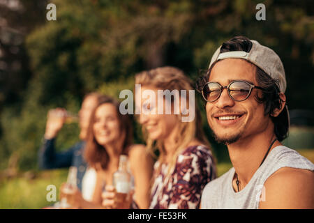 Porträt von glücklicher junger Mann an einem See mit Freunden sitzen. Junge Freunde hängen am See. Stockfoto