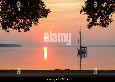 Waterfront-Szene eines Segelbootes bei Sonnenaufgang mit einem Spiegelbild im Wasser. Stockfoto